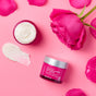 A jar of Andalou 1000 Roses Biome Balancing Day Cream, a smear of cream, and a blooming rose on a pink background.