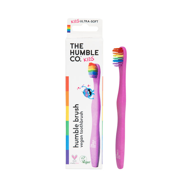A pink Kids Rainbow Brush by The Humble Co. with ultra-soft, rainbow bristles stands by its colorful box featuring a unicorn, eco-friendly icons, and recyclable packaging.