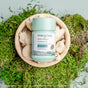 A pouch of True Grace Lion’s Mane Capsules sits atop a bowl of fresh Lion's Mane mushrooms, surrounded by green moss—an inviting display for anyone seeking natural cognitive support.