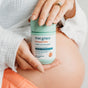 A person with manicured nails holds a bottle of True Grace Prenatal DHA near their bare pregnant belly; the label highlights omega-3 DHA in triglyceride form, supporting optimal brain and eye development.