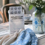 A box of Codeage Molecular Hydrogen, a hydration and magnesium supplement, rests on a table next to a blue-patterned vase with white flowers and matching fabric in a softly lit, cozy setting.