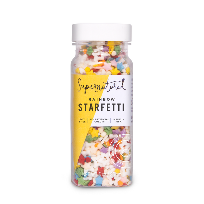 A clear plastic bottle labeled Supernatural Rainbow Starfetti Sprinkle, filled with colorful star-shaped vegan sprinkles made in the USA, featuring plant-based colors, no artificial colors, and soy-free.