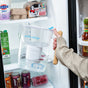 A person holds the Epic Water Filters USA Pure XP Water Filter Pitcher—which is NSF certified and reduces fluoride, PFAS, and parasites—in front of an open refrigerator stocked with yogurt, eggs, drinks, and condiments.