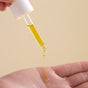 A hand dispenses Wildcraft Regenerate Face Serum, a yellow facial oil, from a dropper onto another palm against a plain beige background.