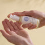 A person pumps Wildcraft’s Calm Face Lotion, a lightweight natural moisturizer, onto their palm against a neutral beige backdrop.
