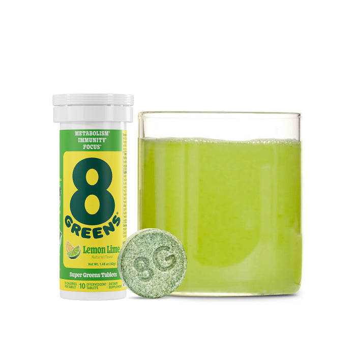 A glass of green liquid sits by a tube labeled 8Greens. In front, a green effervescent tablet with 8G supports metabolism and immunity, making the 8Greens Super Greens Tablet - Lemon Lime a focus and well-being powerhouse.