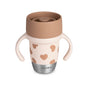 Introducing the BEABA Stainless Steel Learning Cup, Click & Drink: a beige and pink cup featuring two easy-grip handles, brown heart patterns, a brown lid, and a sturdy silver base labeled BÉABA. Designed with a 360° valve-free, spill-proof system for effortless sipping and mess-free learning.