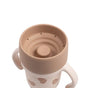 Introducing the BEABA Stainless Steel Learning Cup, Click & Drink—a beige and tan toddler sippy cup adorned with heart patterns. Designed with two easy-grip handles, this cup features a soft, spill-proof rim with small holes for drinking, making it simple and mess-free for little ones to use.