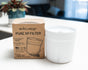 A white Pure XP Replacement Filter by Epic Water Filters USA, designed for advanced water filtration, is displayed next to its brown box marked “PURE XP FILTER” on a white counter, with a blurred plant and sofa in the background.