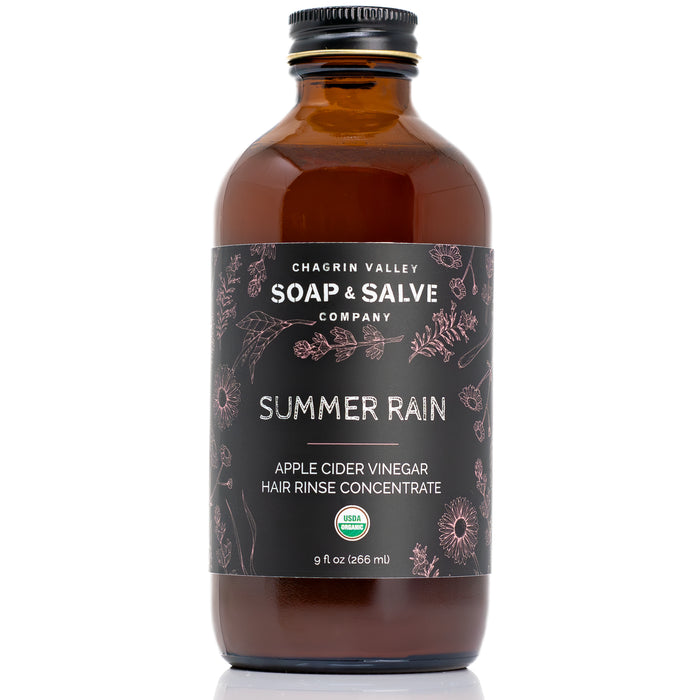 A brown glass bottle labeled Chagrin Valley Soap & Salve Apple Cider Vinegar Hair Rinse features botanical designs and a black cap—an organic clarifying hair care product.