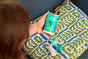 A person holds a container of Aunt Fannie’s Carpet Refresher for Cats over a green and white cushion with a toy mouse and two blue balls nearby.