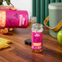 A hand pours Aunt Fannies FlyPunch! Fruit Fly Trap Refill into a matching jar on a wooden countertop with fruit and a green container nearby—an easy, eco-friendly way to reduce plastic use with this refill bottle.