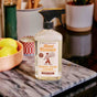 Aunt Fannies Granite + Stone Cleaner, a natural surface spray in bright lemon scent, rests on a marble tray atop a kitchen counter, with lemons and blurred kitchen items in the background.