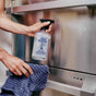 Someone cleans a stainless steel appliance with Aunt Fannies Stainless Steel Cleaner and a blue textured cloth.