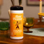 A container of Aunt Fannies Wood Surface Wipes with a lemon scent and no-wax formula sits on a wooden table. The yellow label features a cartoon woman with a mop, set against glassware and candlelight in the background.