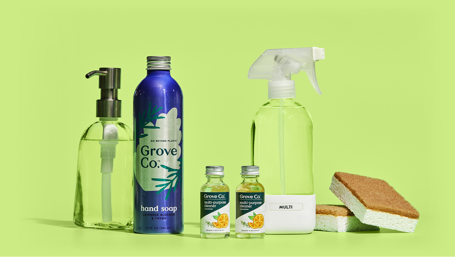 A group of cleaning products and supplies are arranged against a bright green background, including a hand soap dispenser, a reusable spray bottle, a refillable hand soap bottle, two small cleaning concentrate bottles, and two sponges.