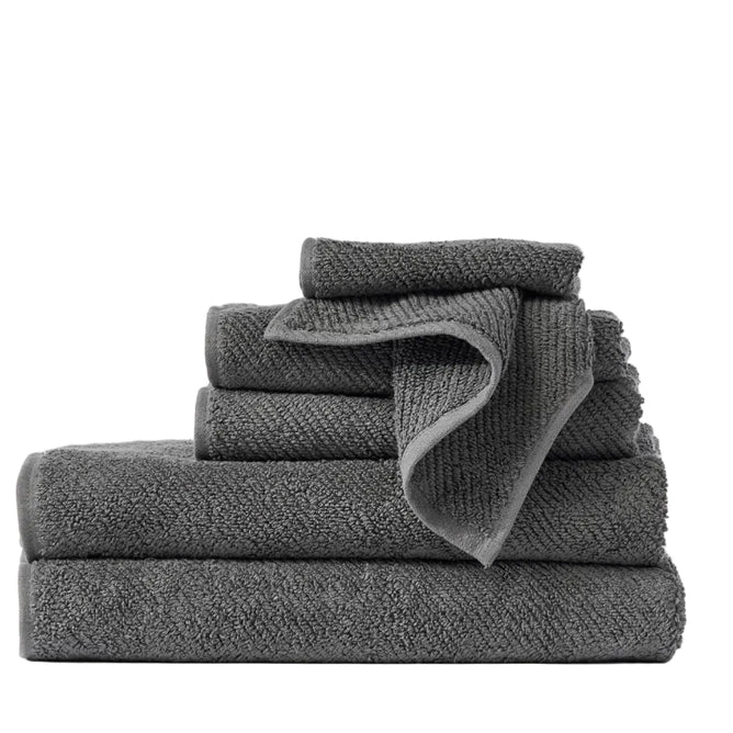 A neatly stacked set of folded Air Weight® Organic Towels by Coyuchi in dark gray, featuring various sizes, is arranged on a light surface with a plain white background.