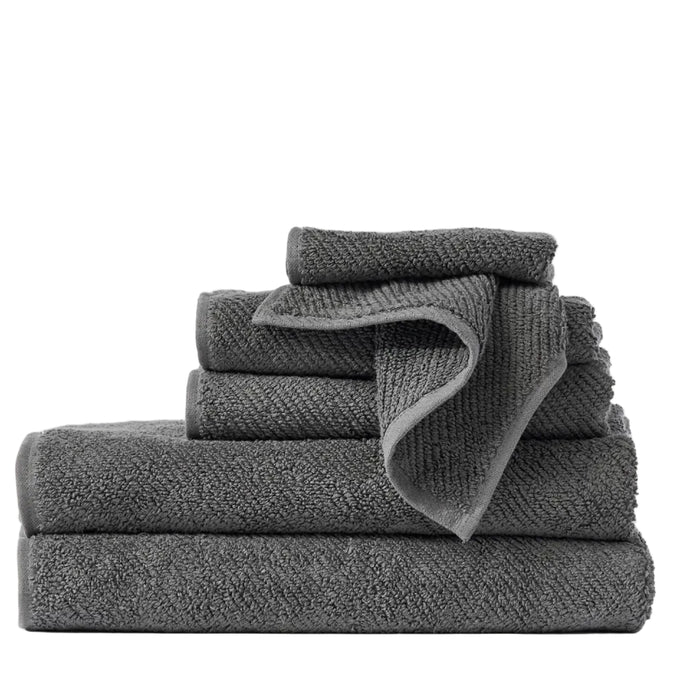 A neatly stacked set of folded Air Weight® Organic Towels by Coyuchi in dark gray, featuring various sizes, is arranged on a light surface with a plain white background.