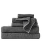 A neatly stacked set of folded Air Weight® Organic Towels by Coyuchi in dark gray, featuring various sizes, is arranged on a light surface with a plain white background.