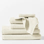 The Coyuchi Oversized Hand Towel from the Air Weight Collection, in cream-colored organic cotton, is shown neatly stacked with a washcloth on top, all set against a plain white background.