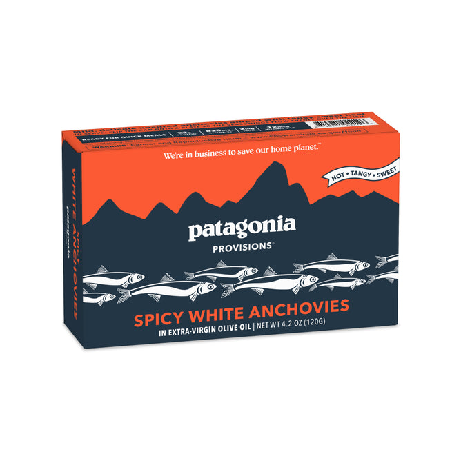A box of Patagonia Provisions White Anchovies Spicy, in extra-virgin olive oil. The dark blue packaging features fish and orange mountains, highlighting the hot, tangy, sweet high-protein flavor.