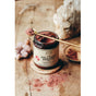 A jar of Anima Mundi COLLAGEN BOOSTER Powder, Superfruit Bliss rests on a wooden surface. A gold spoon holds its vibrant powder above, with some scattered on the table amid crystals and a dish in the background.