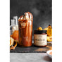A tall chocolate smoothie with vanilla ice cream sits beside a jar of Anima Mundi’s HE SHOU WU, Hair Strength—renowned for hair vitality—on a dark slate surface, with bananas and orange peels in the background.