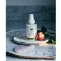 A bottle of Anima Mundi IMMORTELLE Face Cream, Hydrating + Rejuvenative, with a spray nozzle sits on a round white tray beside a pink rose and polished stone, set against a marble background.