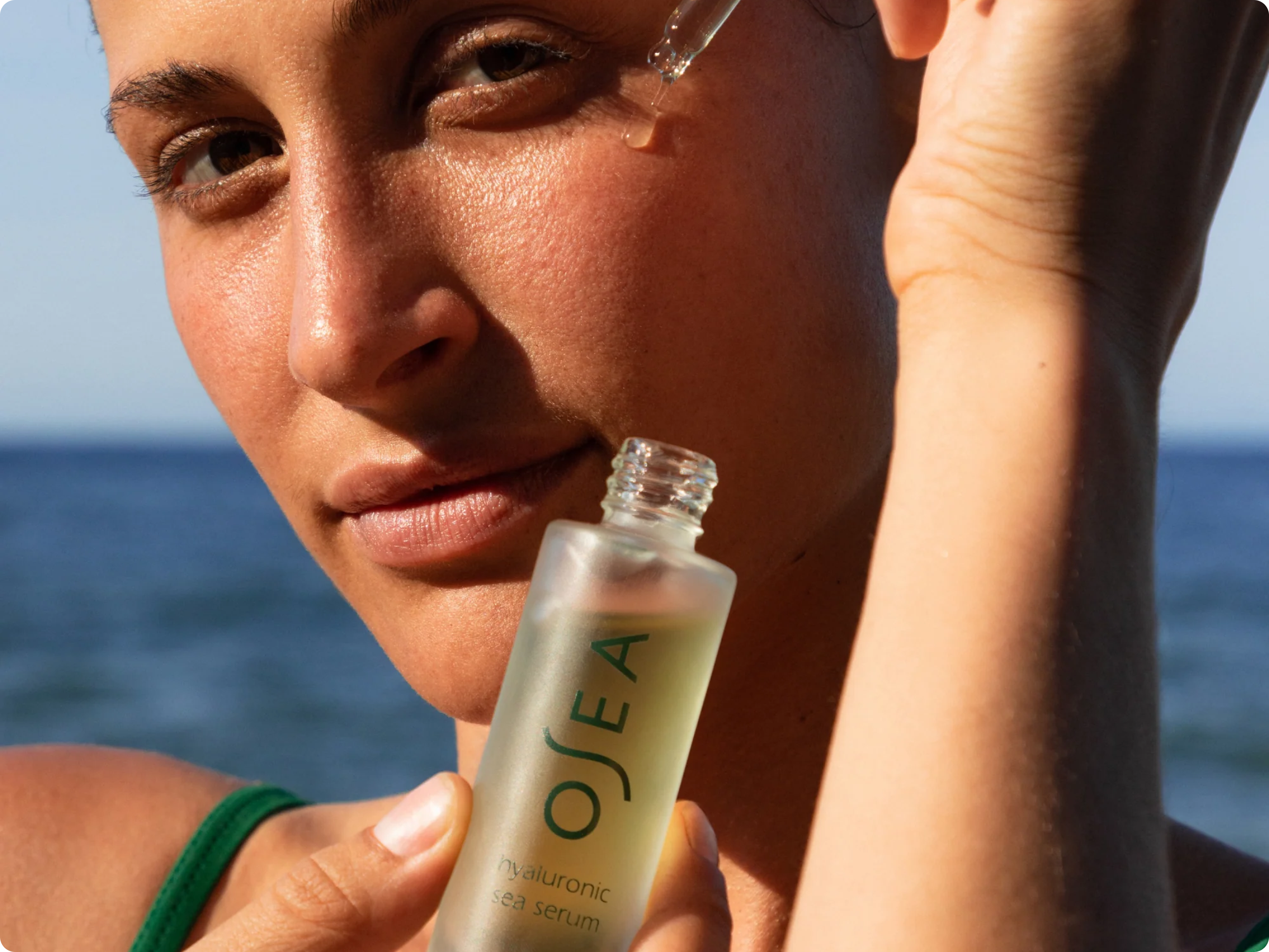 Woman holding a bottle of OJEA skincare product with ocean in the background