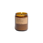 A lit amber jar candle from P.F. Candle Co., labeled Soy Wax Candle and featuring a beige paper tag, sits elegantly on a white surface.