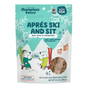 A blue and white bag of Shameless Pets Dog Treats - Après Ski and Sit, made with real duck, features two cartoon dogs in winter outfits snacking together amid a snowy mountain and tree backdrop.