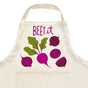 A kitchen essential, The Neighborgoods Apron features a playful beet print with slices and leaves plus “BEET it” in purple and pink letters.
