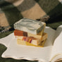 Four colorful, rectangular bars from the Pacha Soap Co. Bar Soap Set – Autumn Heirlooms Collection are stacked on top of an open lined notebook, with a plaid blanket in the background.