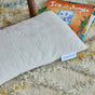 An Avocado Toddler Pillow in cream rests on a textured rug next to a children’s book, Ice in the Jungle, partially visible in the background.