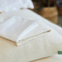 A set of Avocado Organic Indian Cotton 400 TC pillow cases with a sateen finish is neatly folded on the bed, resting atop a textured, cream-colored pillow featuring a green tag.