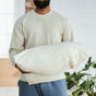 A person in a light long-sleeve shirt and blue pants holds a white pillow in a bright room, featuring an Avocado Organic Indian Cotton 400 TC Pillow Case Set on the bed with GOTS certified sheets and soft natural light.