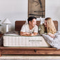 A smiling man and woman lie on their stomachs on an Avocado Green Mattress in a cozy, modern bedroom, enjoying its pressure-relieving comfort as they look at each other.