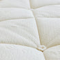 Close-up of the Luxury Organic Mattress by Avocado Green Mattress, highlighting its soft, cream-colored, quilted surface with textured organic fabric and a button tuft at the intersection of stitched lines.