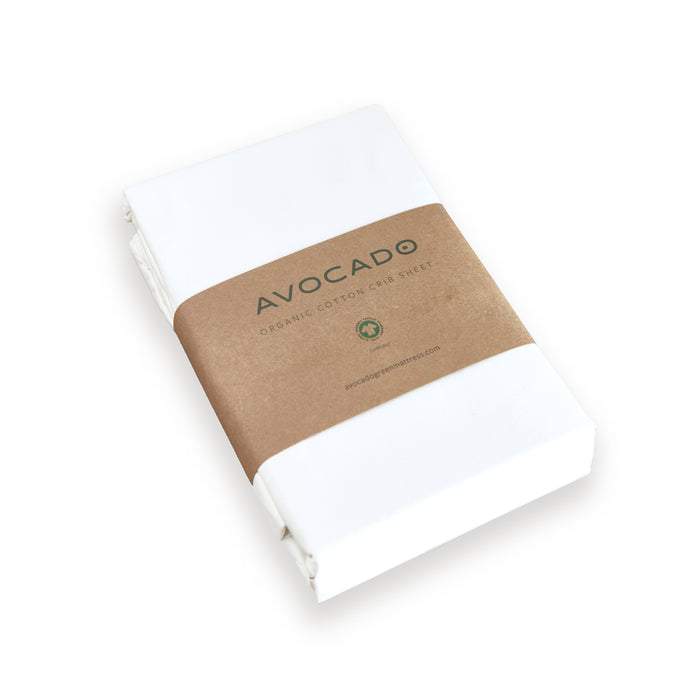 A neatly folded Avocado Organic Cotton Crib Sheet, wrapped with a brown paper band and made from GOTS certified organic cotton, is displayed on a plain white background.