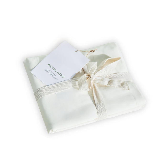 A folded set of Avocado Organic Indian Cotton 400 TC Pillow Case Set in natural color, elegantly tied with a ribbon and featuring a white Avocado brand tag.