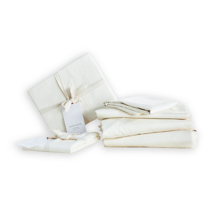 The Avocado Organic Indian Cotton 400 TC Sheet Set in Natural, GOTS certified, includes neatly folded sheets and pillowcases with tags and ribbon, displayed on a white background.