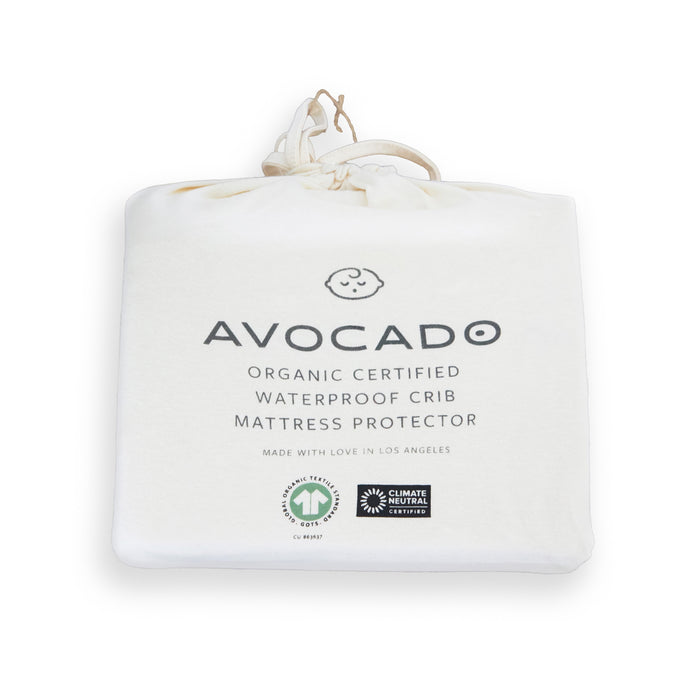 The Avocado Organic Crib Waterproof Mattress Protector comes in a white fabric bag with minimalist text and icons, drawstring closure, eco-friendly certification logos, and is MADE SAFE certified.