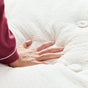 A hand presses down on the Avocado Green Ultra Plush Mattress by Avocado Green Mattress, creating a visible indentation in its soft, white natural latex surface.