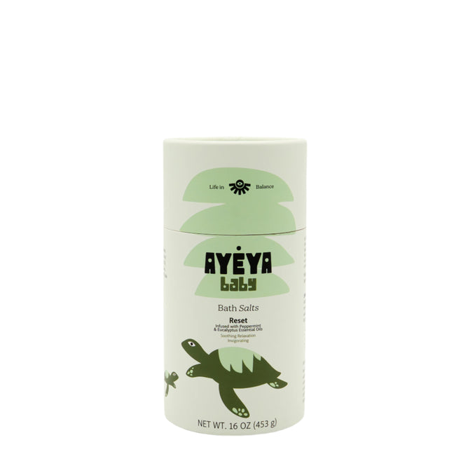 A 16 oz (453 g) cylindrical container of Ayeya Baby Bath Salts with a light green design, turtle illustration, and “Reset” text. These bath salts help soothe tension and hydrate baby skin.