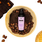 An Ayeya Moisturizing Body Wash rests in a wooden bowl with brown cloth and shea nuts, surrounded by more shea nuts and a brown towel, capturing the calming scent and richness of essential oils.
