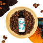 A bottle of TABS Liquid by Ayeya sits in a wooden bowl filled with shea nuts. More shea nuts, a brown towel, and a colorful fan surround it—evoking skin balance inspired by African Black Soap on a white background.
