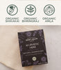 A Natural Shampoo Bar by Chagrin Valley Soap & Salve rests on a beige textured cloth, with icons above highlighting organic shikakai, coconut oil, bhringraj, and amla ingredients.