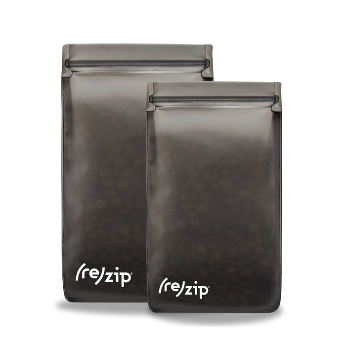 The Coffee/Tea Storage Bag Kit includes two reusable, semi-transparent dark gray bags with the brand (re)zip in white at the bottom. They stand upright and have a zip-lock top, perfect for maintaining freshness of coffee beans or tea leaves.