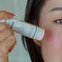 A person applies Baeo Bare Tint - Mineral Lip + Cheek Tint to their cheek, with the image highlighting the hand and cheek and showcasing its natural mineral color used as blush.