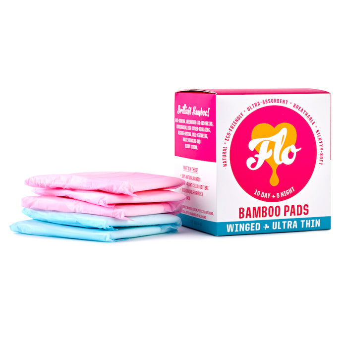 The Here We Flo Bamboo Pads with Wings, Day + Night Combo Pack, feature a box beside three wrapped pads in pink and blue packaging. They offer eco-friendly, hypoallergenic period protection thats ultra-absorbent, breathable, silky soft, and compostable.